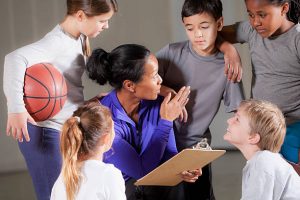 Children (7-9 years) with basketball coach (30s) in gym.